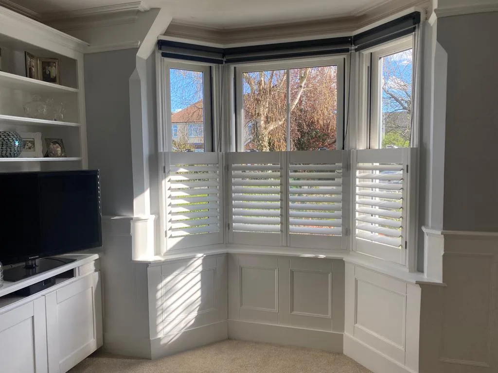 White plantation shutters installed in a bay window in a living room.