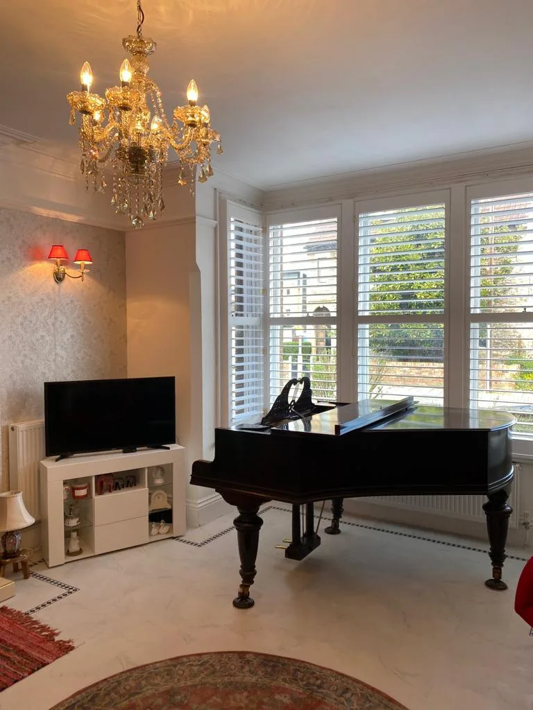 White plantation shutters installed in a bay window in a living room with a grand piano.