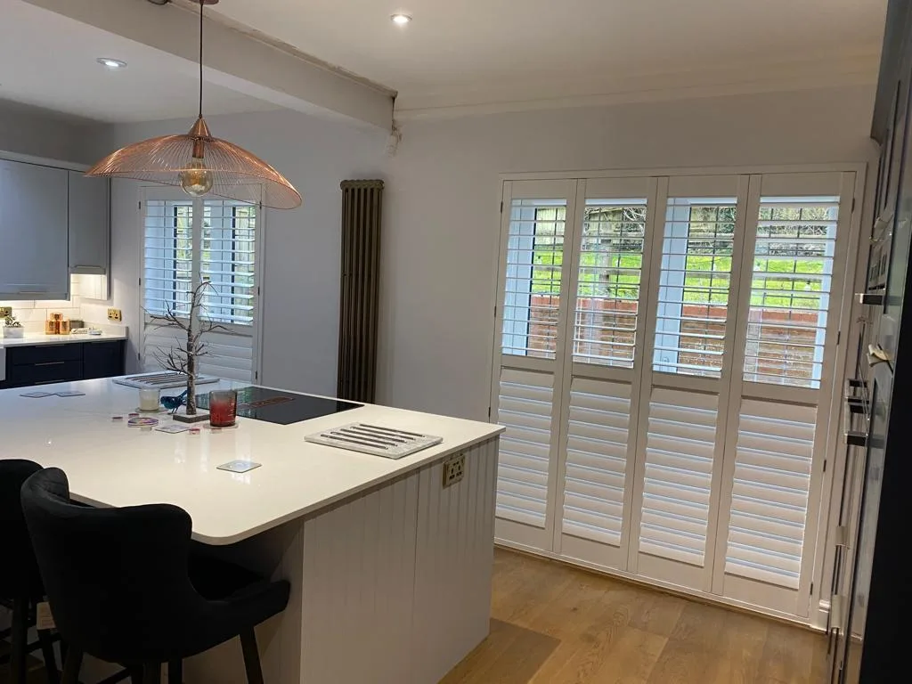 White full height plantation shutters installed on French doors in a modern kitchen with an island.