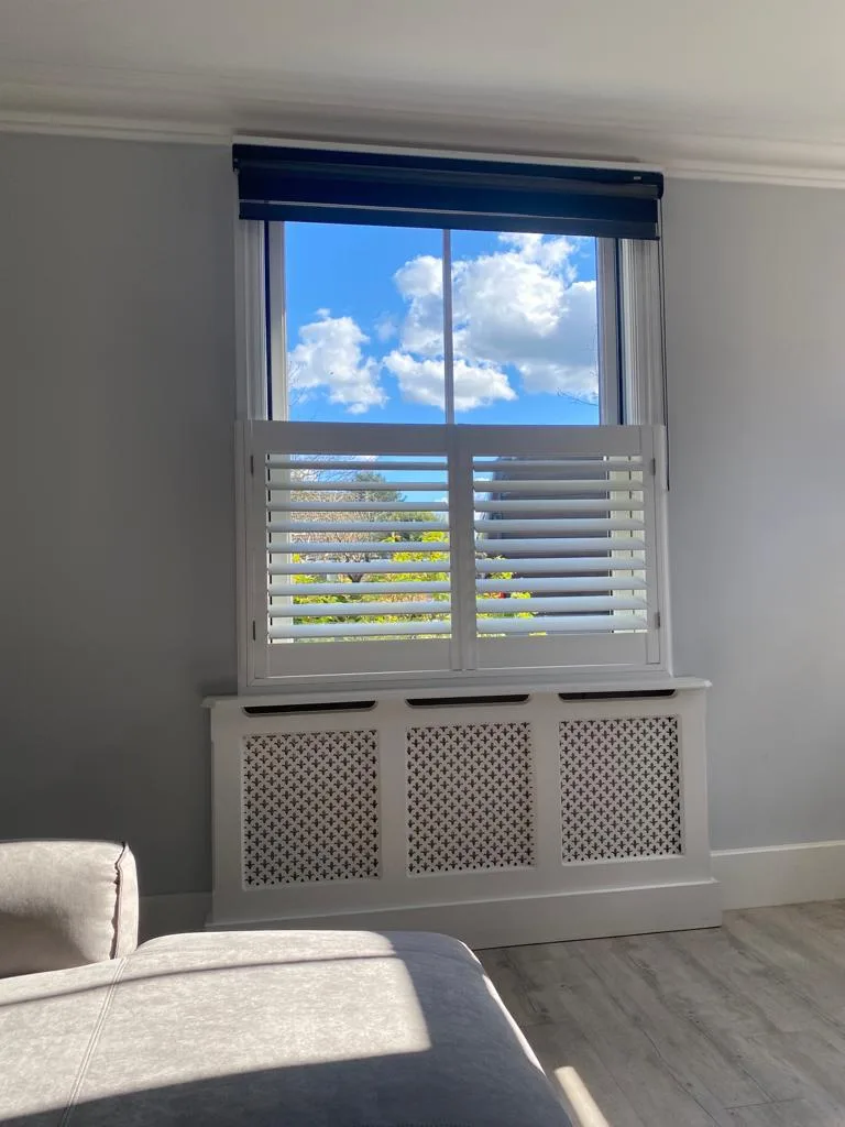 Café style shutters in a living room, with a dark roller blind at the top of the window.