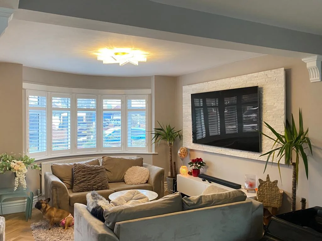 White plantation shutters installed in a bay window in a modern living room.