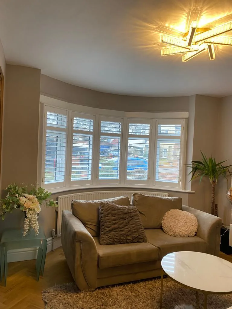 White plantation shutters installed in a bay window in a modern living room.