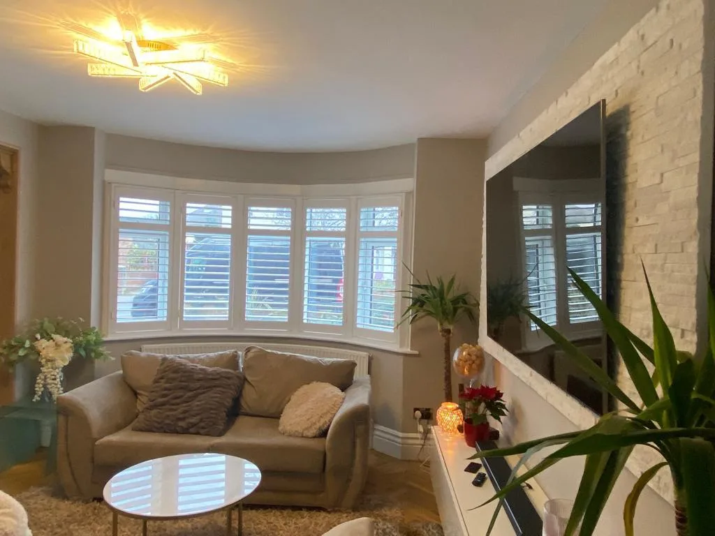White plantation shutters installed in a bay window in a modern living room.