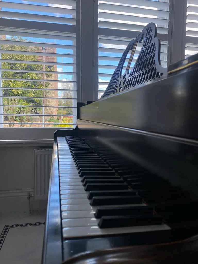 Full height shutters in cream, with a beautiful view of a garden and a piano in the foreground.
