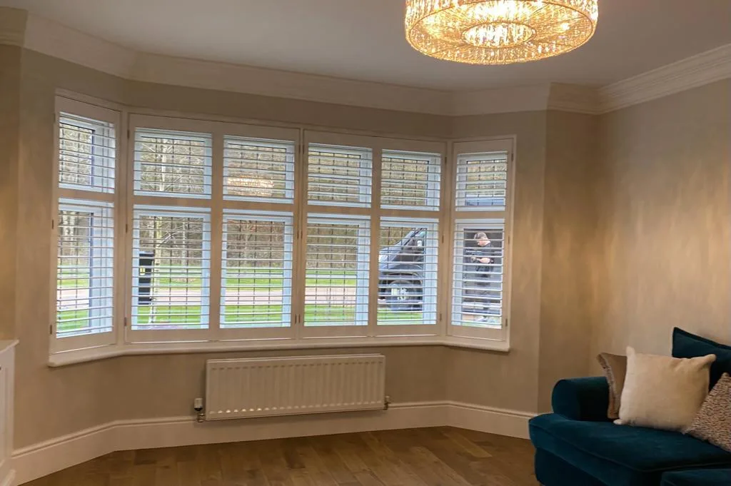 White full height shutters in a modern bay window in a living room.