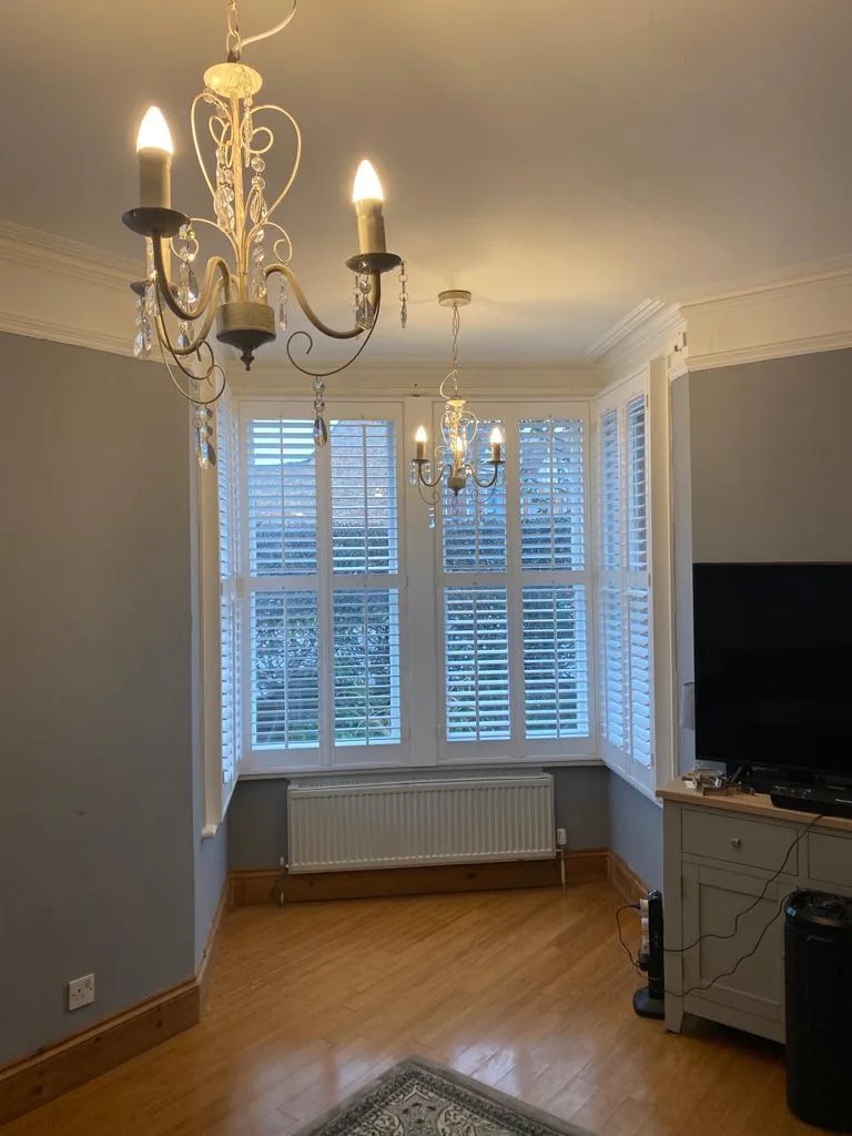 White plantation shutters in a living room bay window.