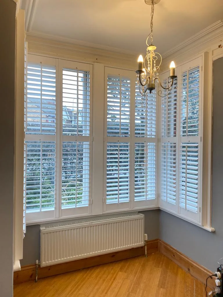 White full height plantation shutters installed in a bay window in a living room.
