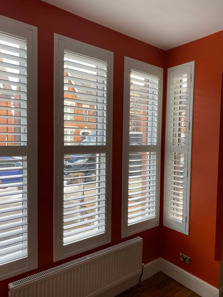 White full height plantation shutters in a living room with vibrant orange walls.