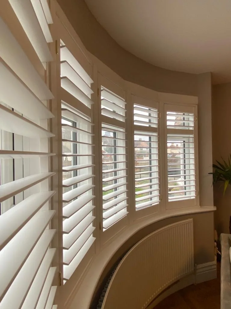 White full height plantation shutters installed in a curved bay window in a living room.