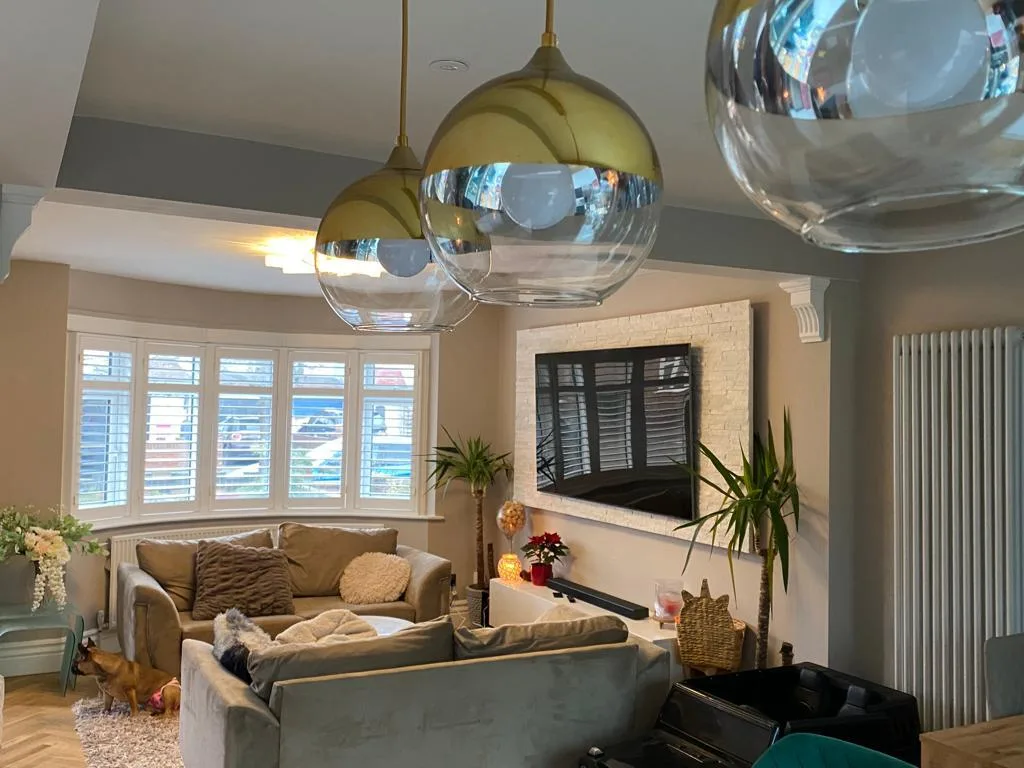 White plantation shutters installed in a bay window in a modern living room.