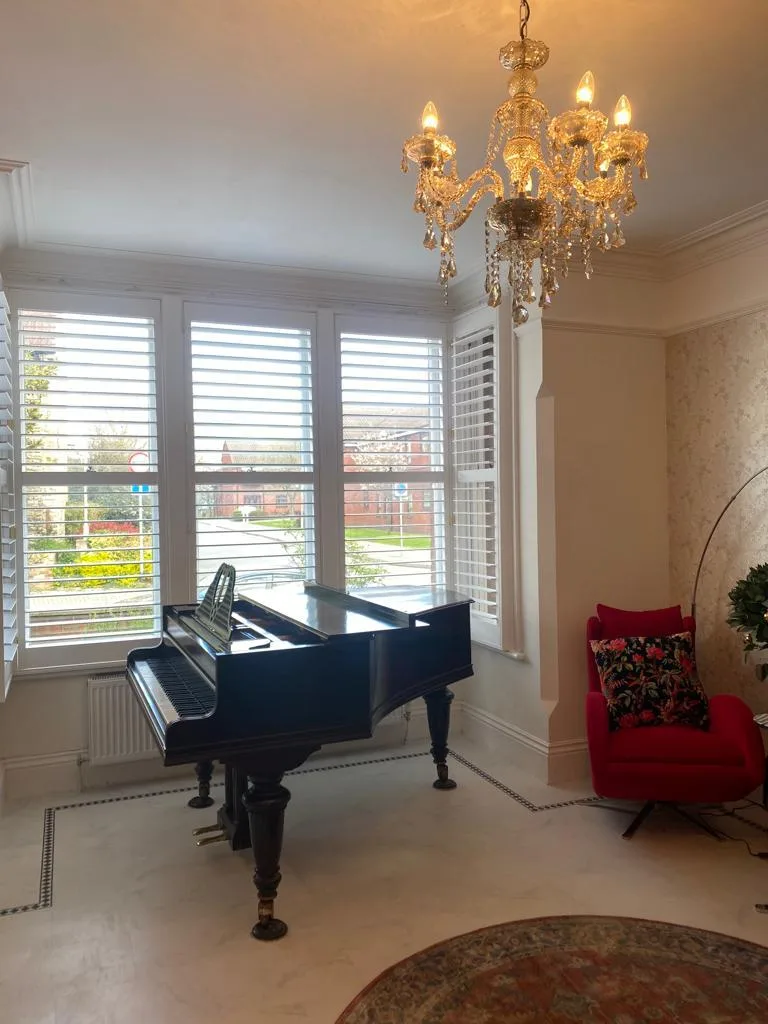 White plantation shutters in a bay window of a living room with a grand piano.