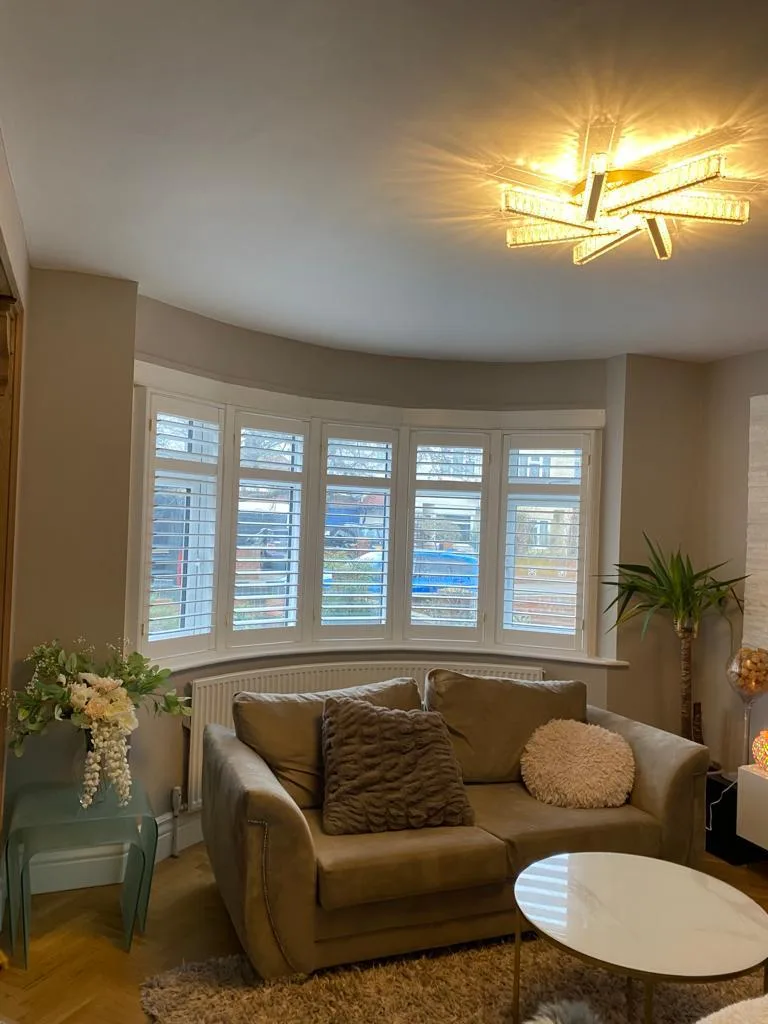 White plantation shutters installed in a bay window in a living room.