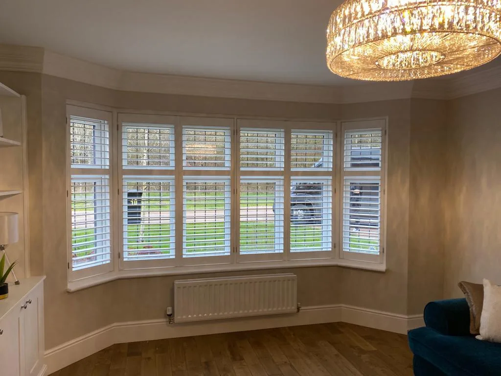 White full height plantation shutters installed in a living room bay window.