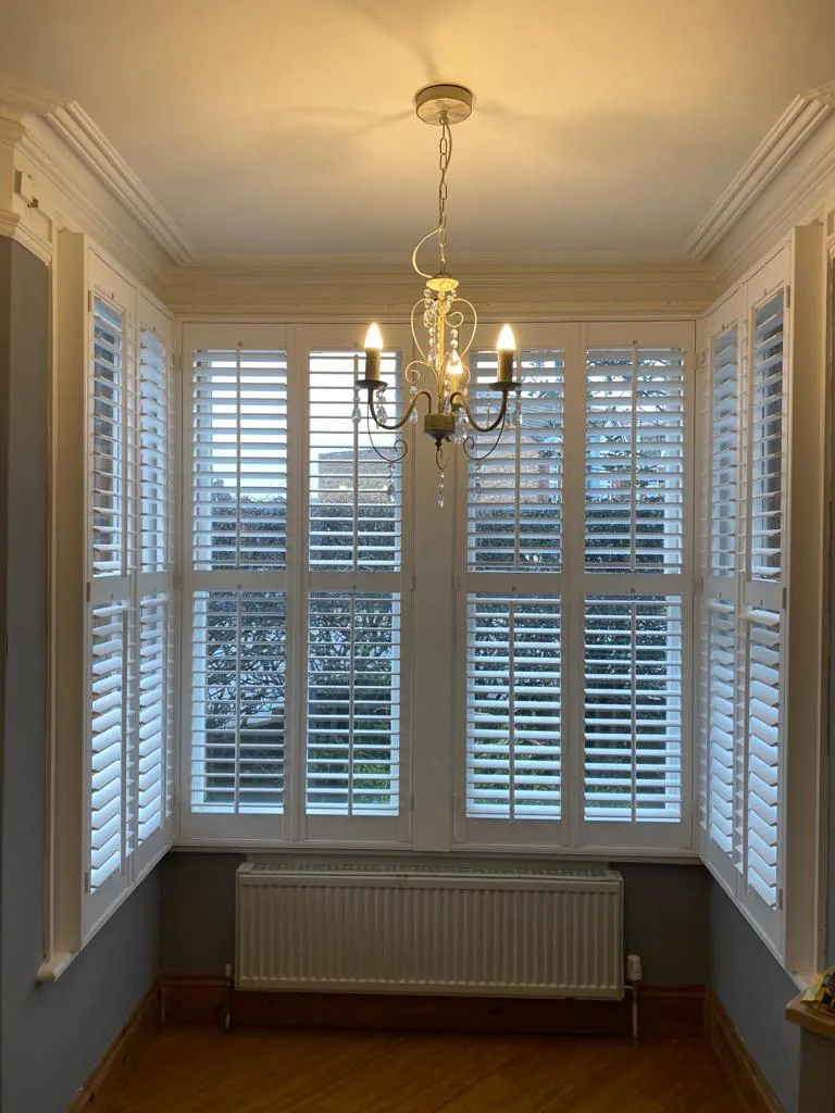 White full height plantation shutters installed in a bay window in a living room.