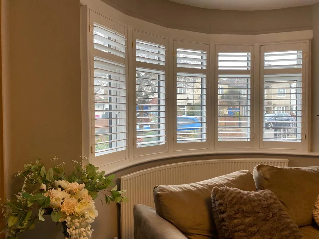White full height plantation shutters installed in a bay window in a living room.