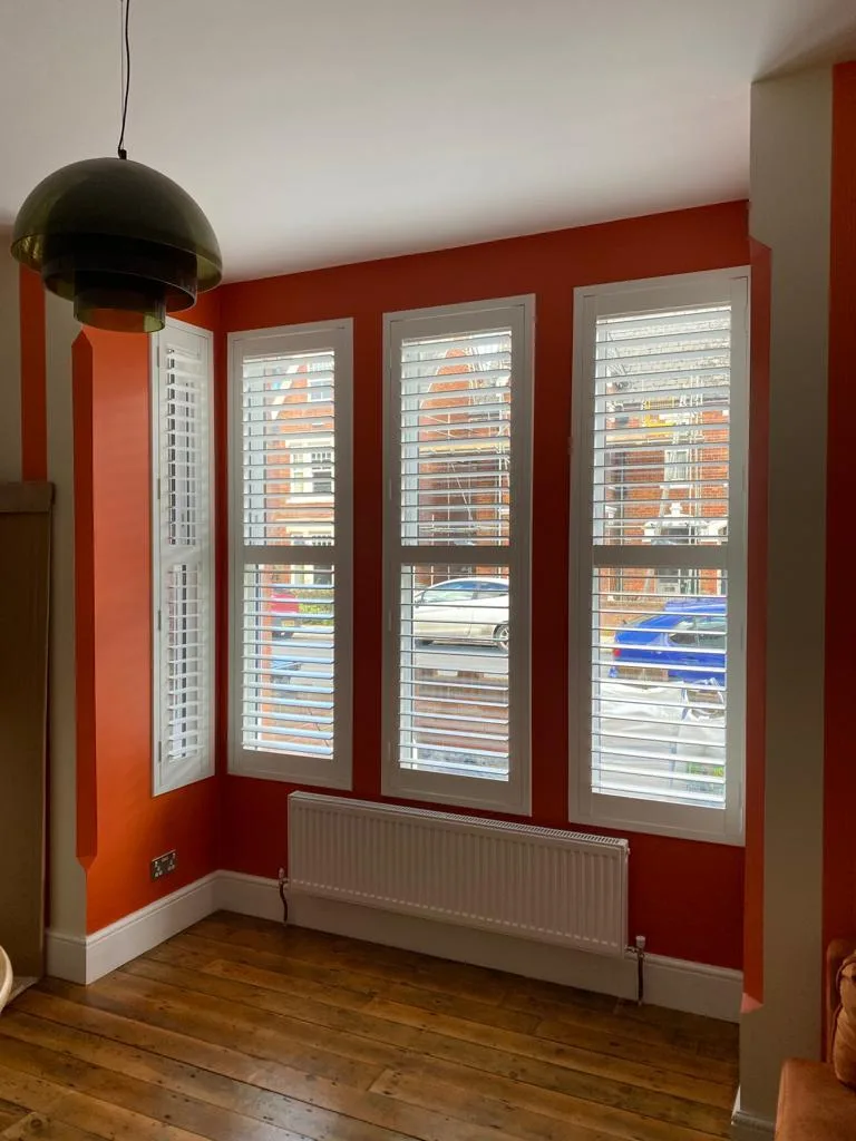 Living room with full height white plantation shutters installed on multiple windows.